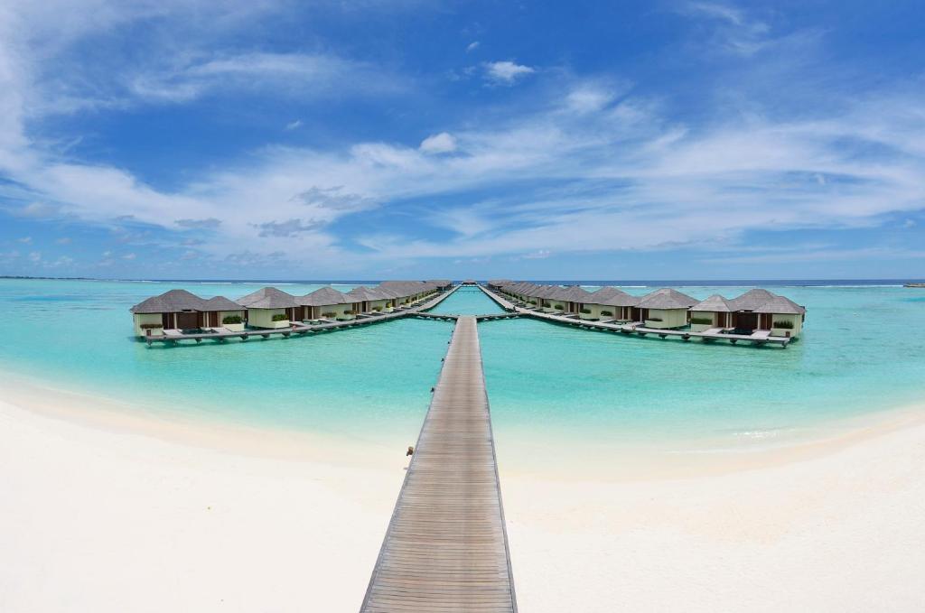 Rows of thatched overwater villas linked by a boardwalk over a turquoise lagoon