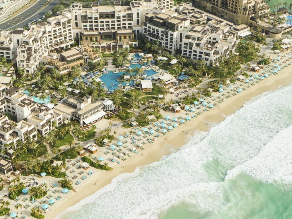 Aerial view of a beachfront resort with pools, cabanas and rows of parasols along the sand