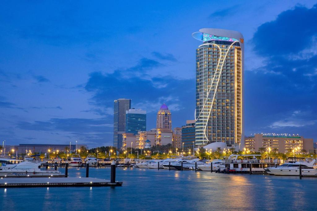 Illuminated hotel tower overlooking a marina lined with moored boats at dusk