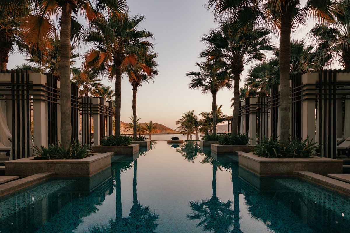 A palm-lined reflecting pool at Jumeirah Muscat Bay at first light, with the Omani headland beyond
