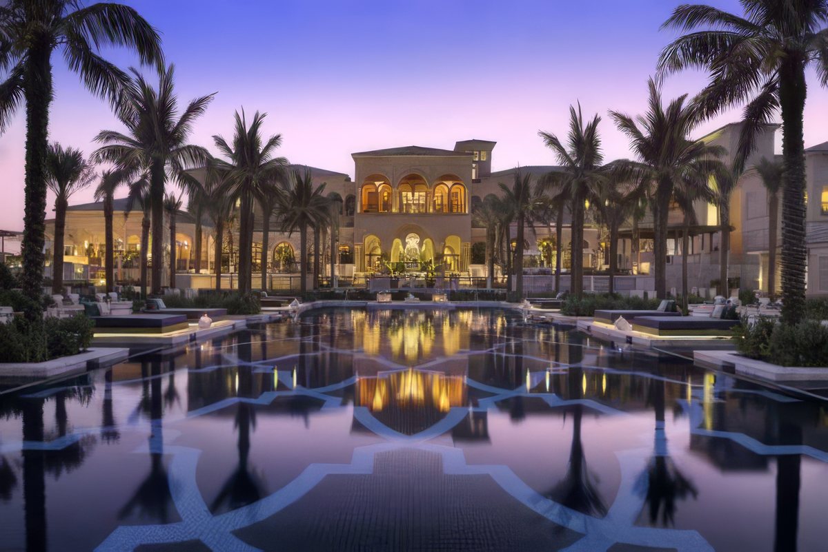 One&Only The Palm at dusk, the arcaded main building reflected in a long formal pool lined with palms
